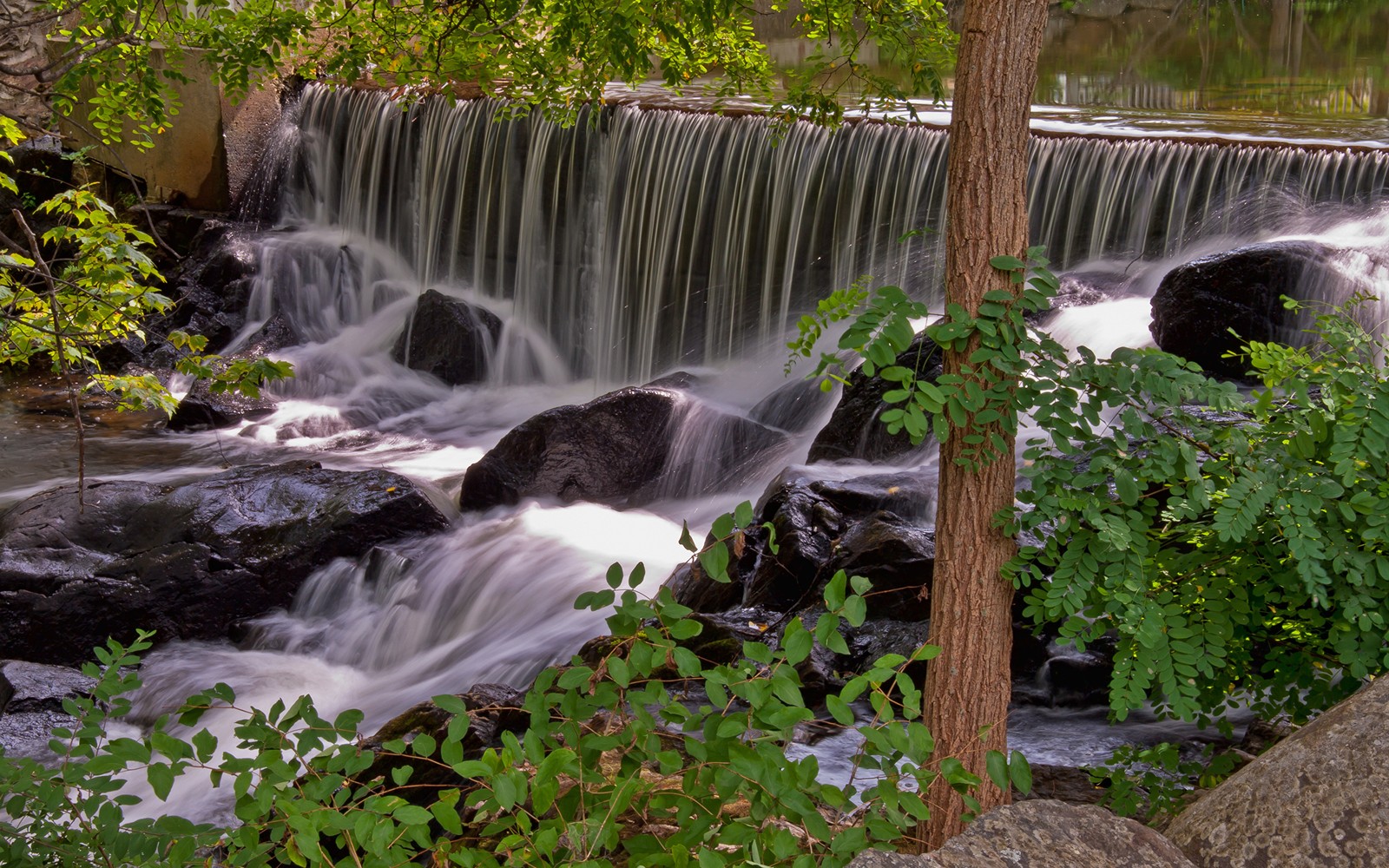 Hay una cascada que fluye sobre rocas en el agua. (cascada, recursos hídricos, cuerpo de agua, naturaleza, agua)