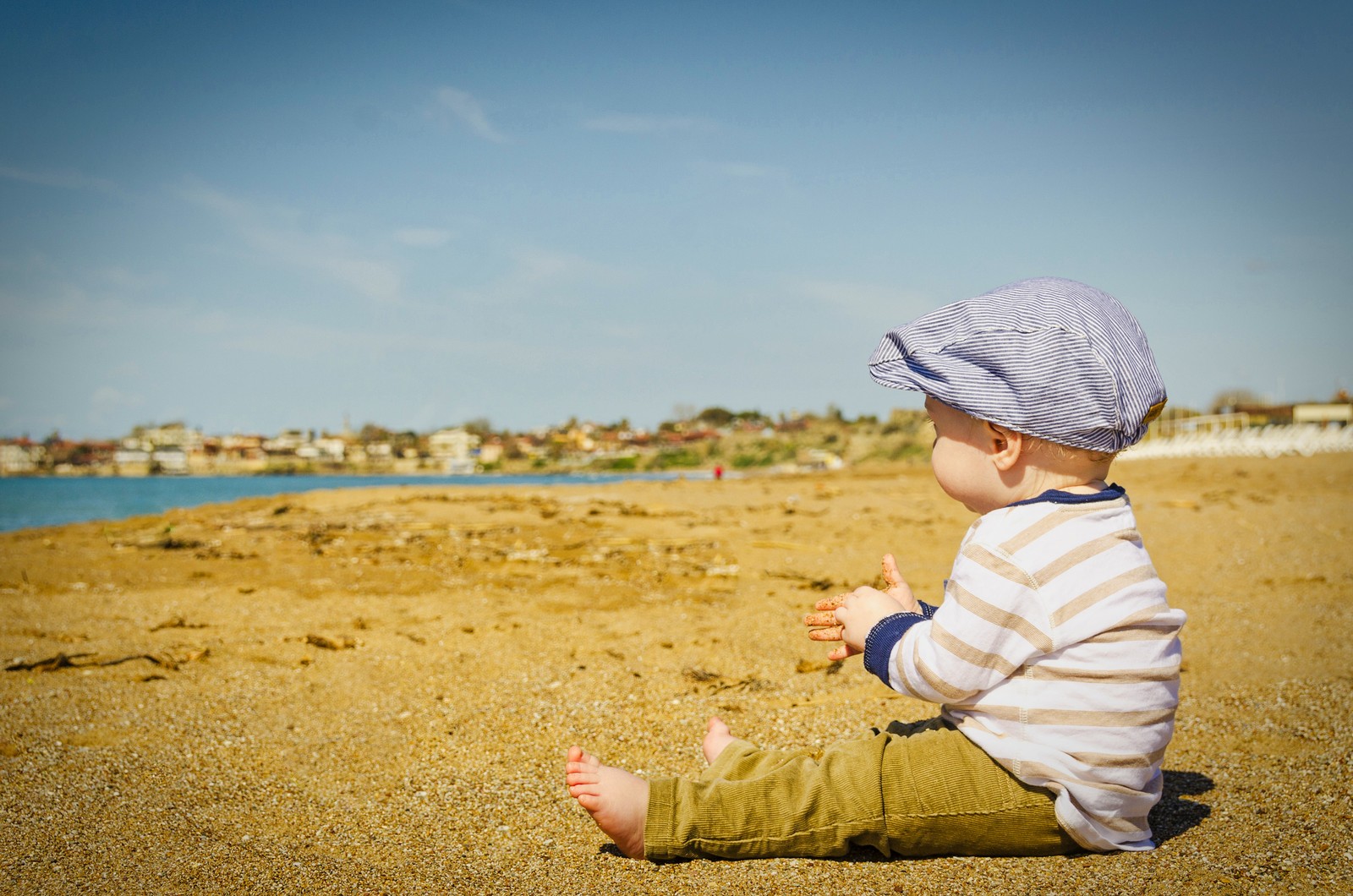 Um bebê sentado na praia com um chapéu (garoto fofo, praia, criança fofa, toddler, criança brincando)