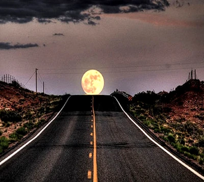 A wide, winding road stretches toward a large, glowing moon on the horizon, set against a dramatic sky.