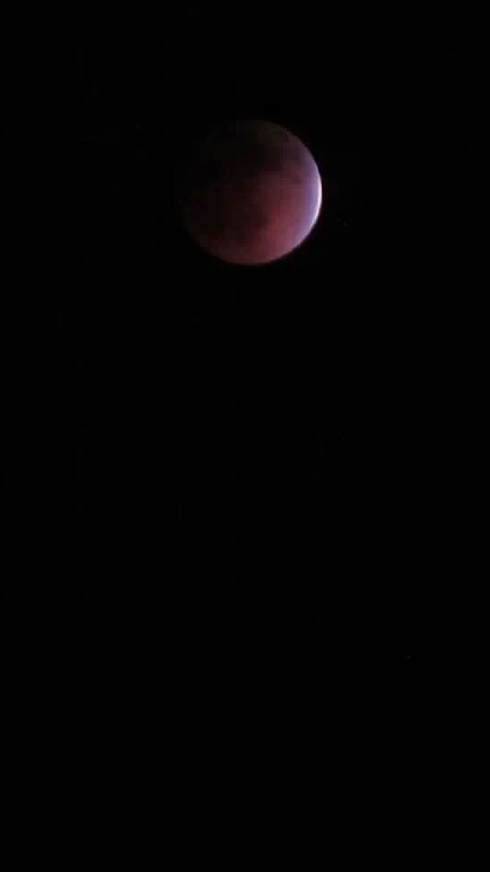 Une lune rouge est visible dans le ciel sombre au-dessus d'une ville (lune, nuit, rouge)