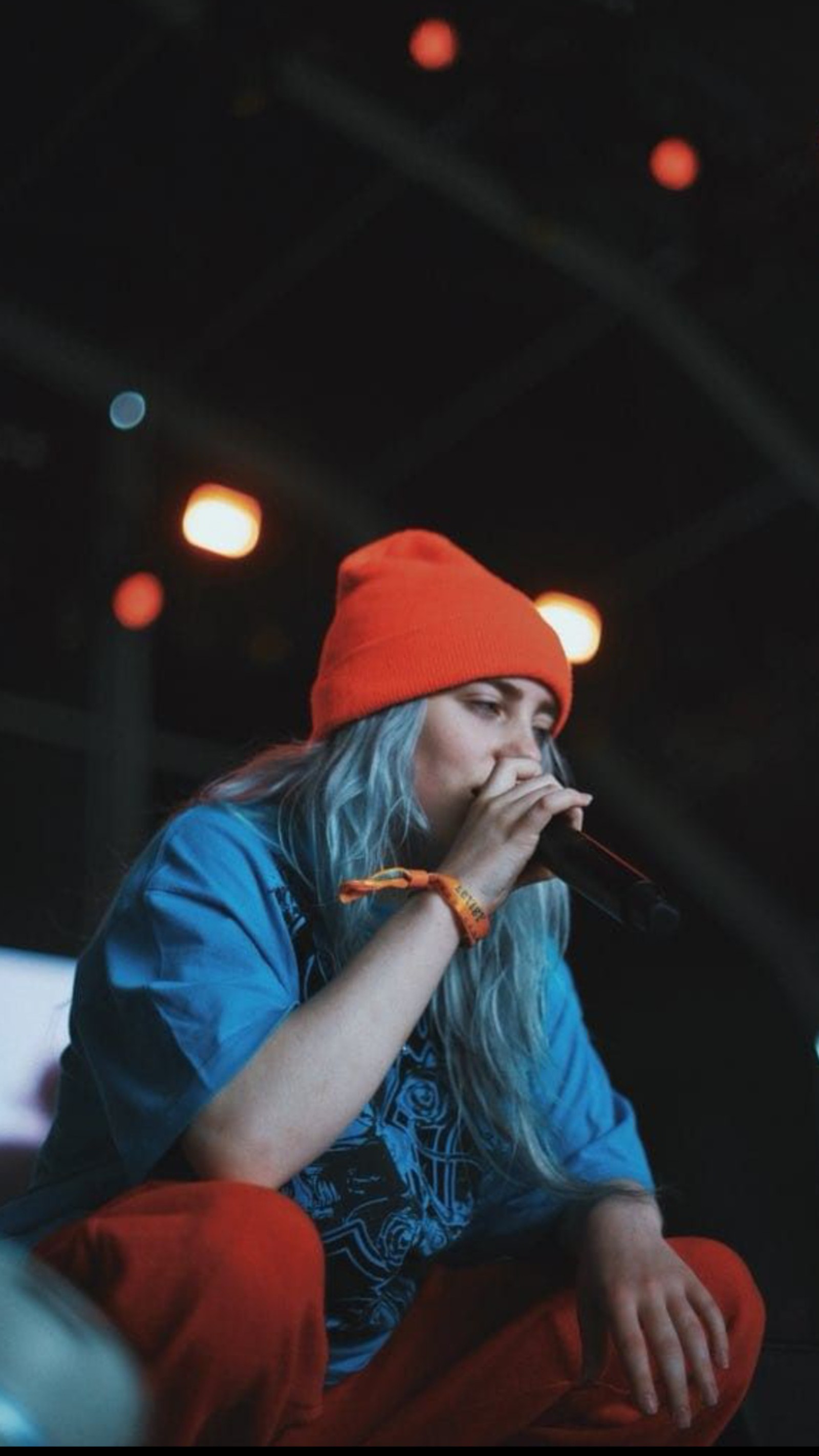 Verschwommenes bild einer frau mit langen weißen haaren und rotem hut auf einer bühne (billie eilish, niedlich, singen)