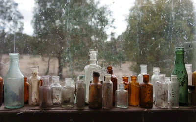 Array de bouteilles en verre vintage sur un rebord de fenêtre poussiéreux.