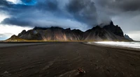 Mystical Highland Landscape: Dramatic Mountain Range Amidst Dark Clouds and Serene Waves