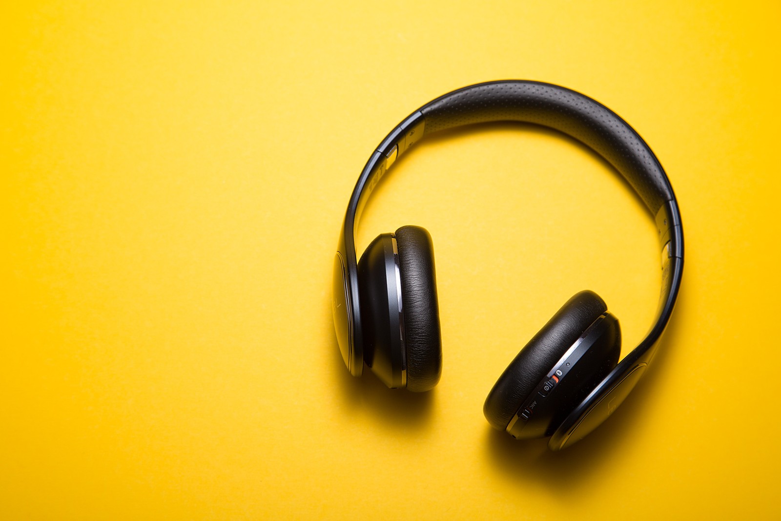 A close up of a pair of headphones on a yellow surface (headphones, headset, yellow, audio equipment, technology)