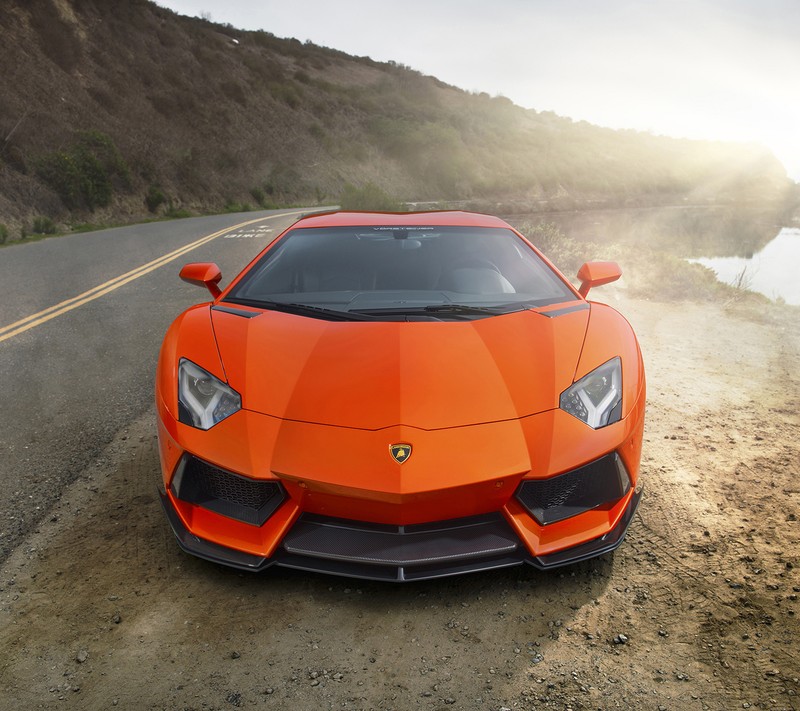 A close up of a orange sports car driving down a road (aventador, front view, lamborghini, vorsteiner)