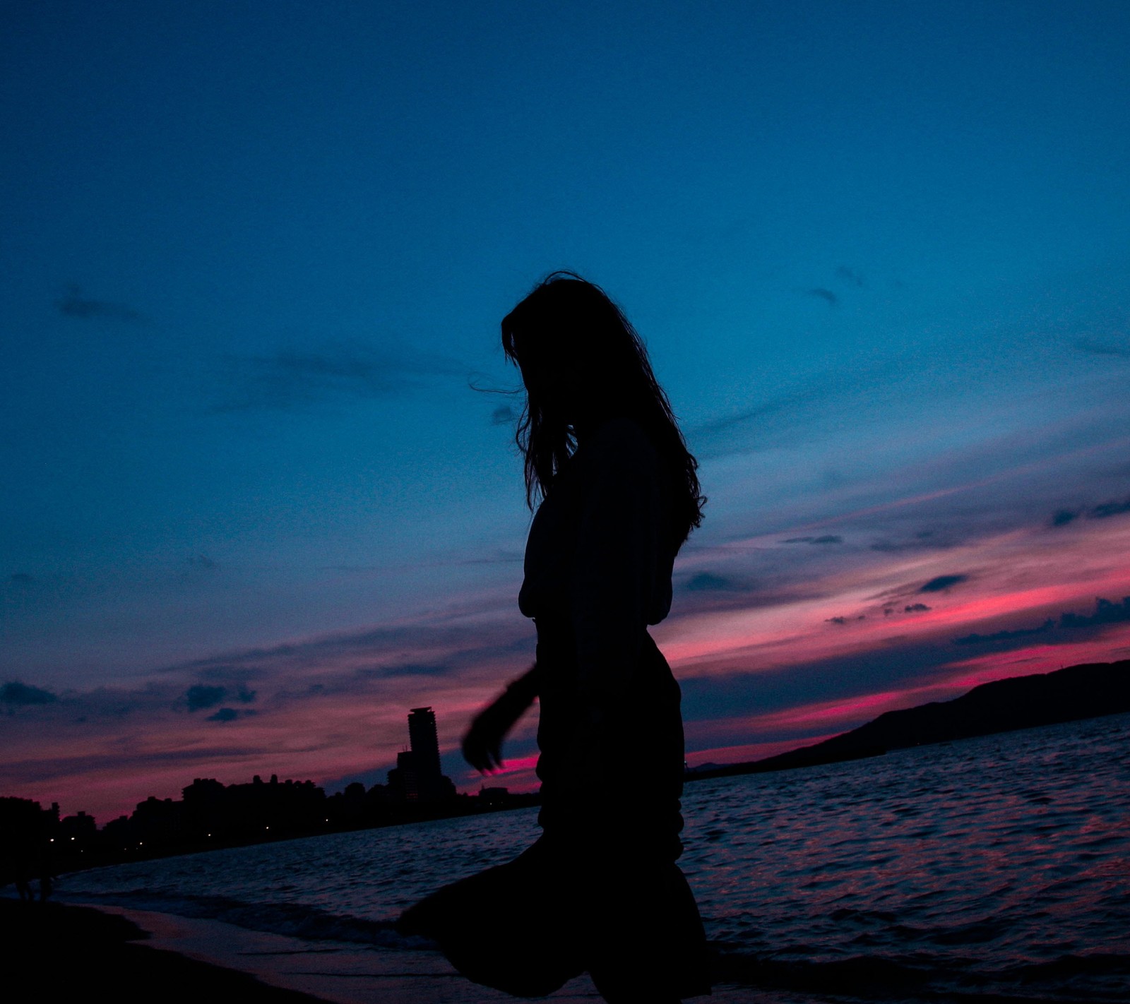 Araffe walking on the beach at sunset with a bottle of water (black, galaxy, girl, night, sea)