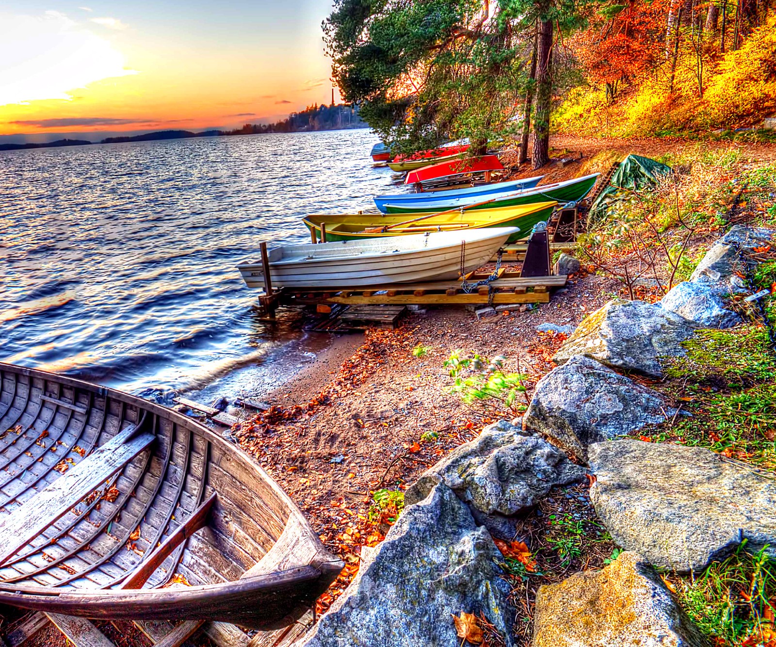 Barcos estão alinhados na costa de um lago ao pôr do sol. (barcos, lago, natureza, por do sol, água)