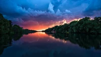 Ruhiger Fluss bei Dämmerung mit Reflexionen und dramatischem Himmel