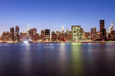 Beleuchtete Skyline von New York City bei Dämmerung mit Reflexionen im Wasser