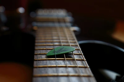 Close-up of a green guitar pick resting on the strings of an acoustic guitar, highlighting the craftsmanship of the instrument and its musical potential.