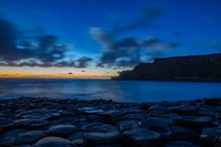 Sonnenuntergang über dem Ozean mit hexagonalem Ufer und dramatischem Himmel