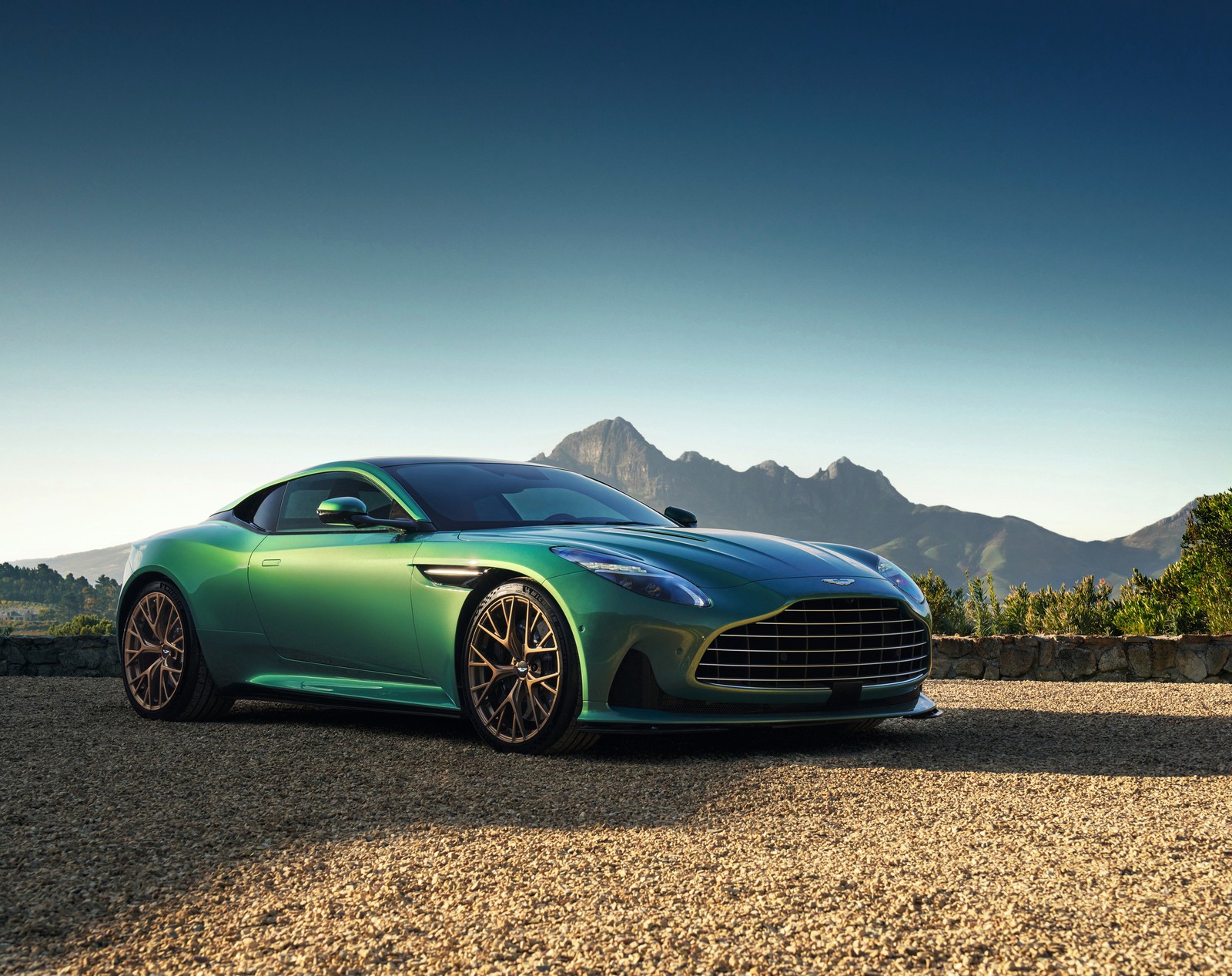 Une voiture verte garée sur un terrain de gravier avec des montagnes en arrière-plan (aston martin db12, haute performance, voitures de sport, supersportive, 5k)