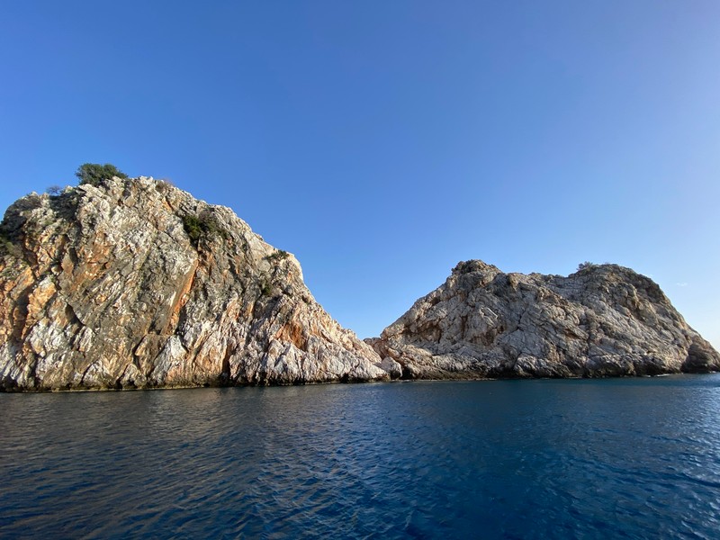 Вид на скалистый остров с несколькими мелкими камнями в воде. (море, вода, водные ресурсы, гора, природный пейзаж)