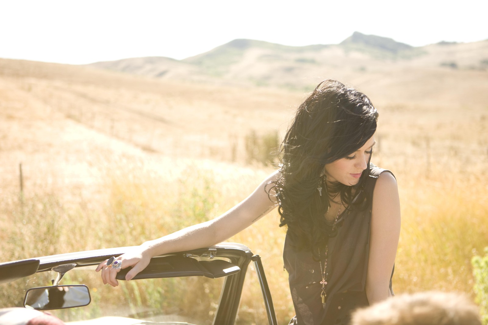 Woman leaning on the hood of a car with a man looking at her (katy perry, sunlight, grass, summer, sitting)