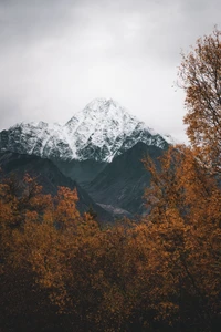 Snow-capped peaks rise above vibrant autumn foliage in a serene alpine landscape.