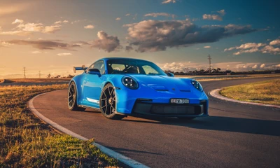 2021 Porsche 911 GT3 PDK в ярко-синем цвете, запечатленный на извивающейся дороге на закате.