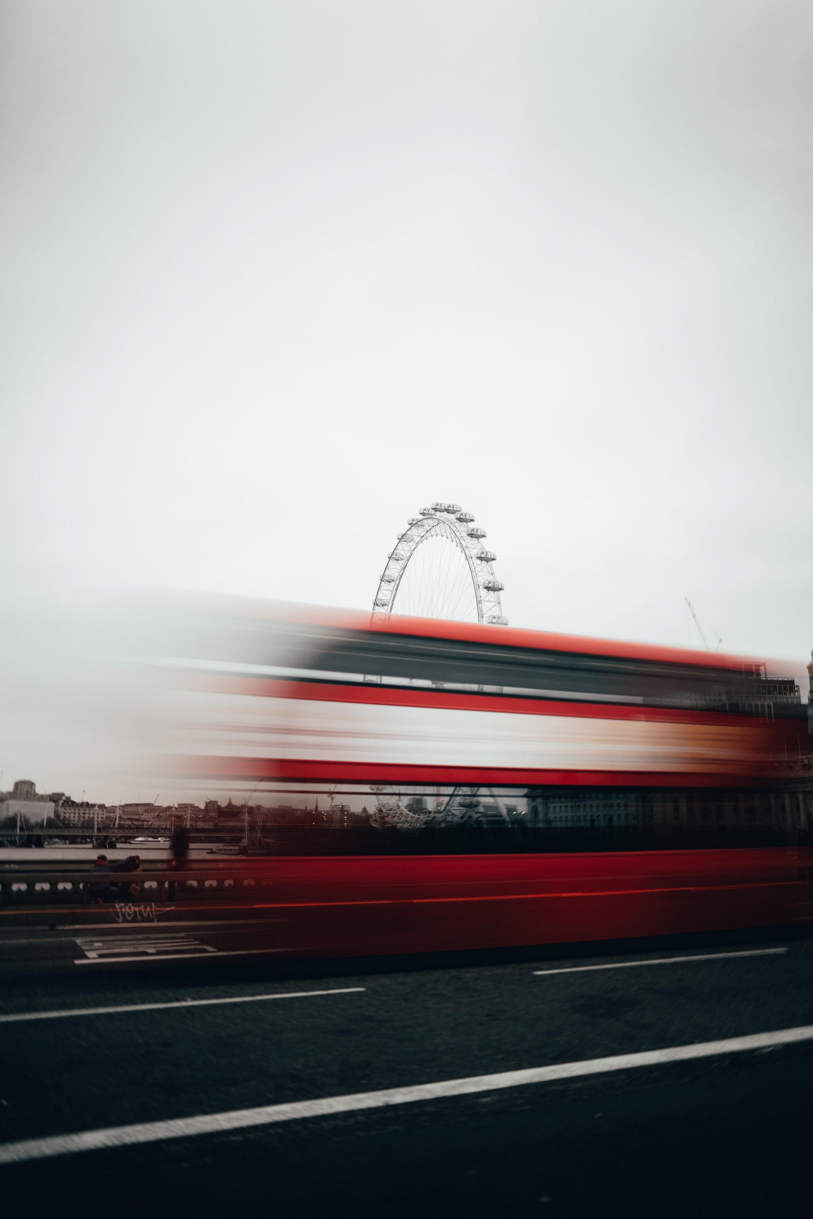 Vue aérienne d'un bus passant devant une grande roue au loin (rouge, transport, nuage, route, architecture)