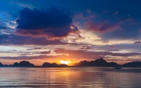 Atardecer sobre la bahía de Bacuit, con montañas en silueta y un paisaje marino tranquilo que refleja tonos vibrantes en el cielo nublado.