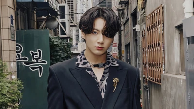 Jungkook de BTS se tient avec confiance dans un élégant costume noir avec une chemise à imprimé léopard, entouré d'un décor urbain.