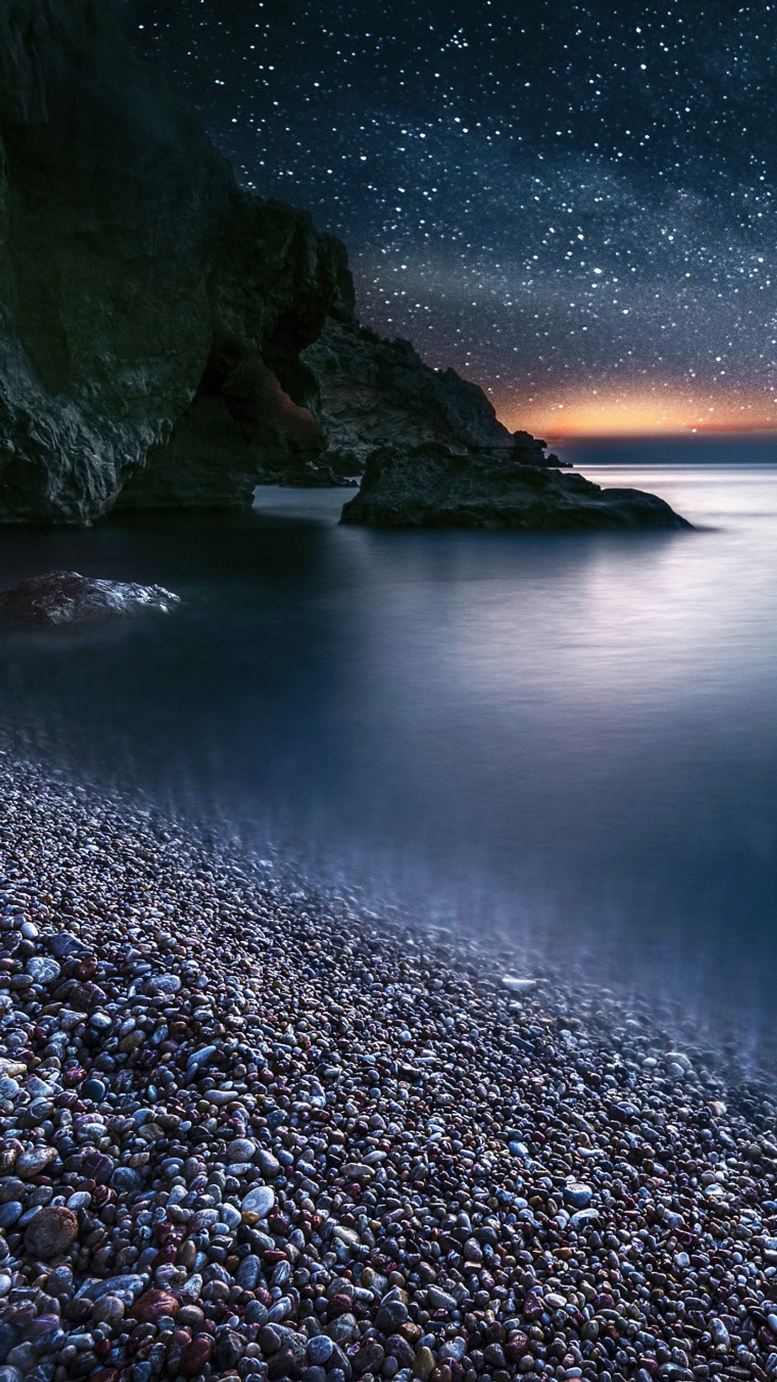 Céu noturno estrelado sobre uma praia rochosa com um corpo de água (preto, paisagem, noite)