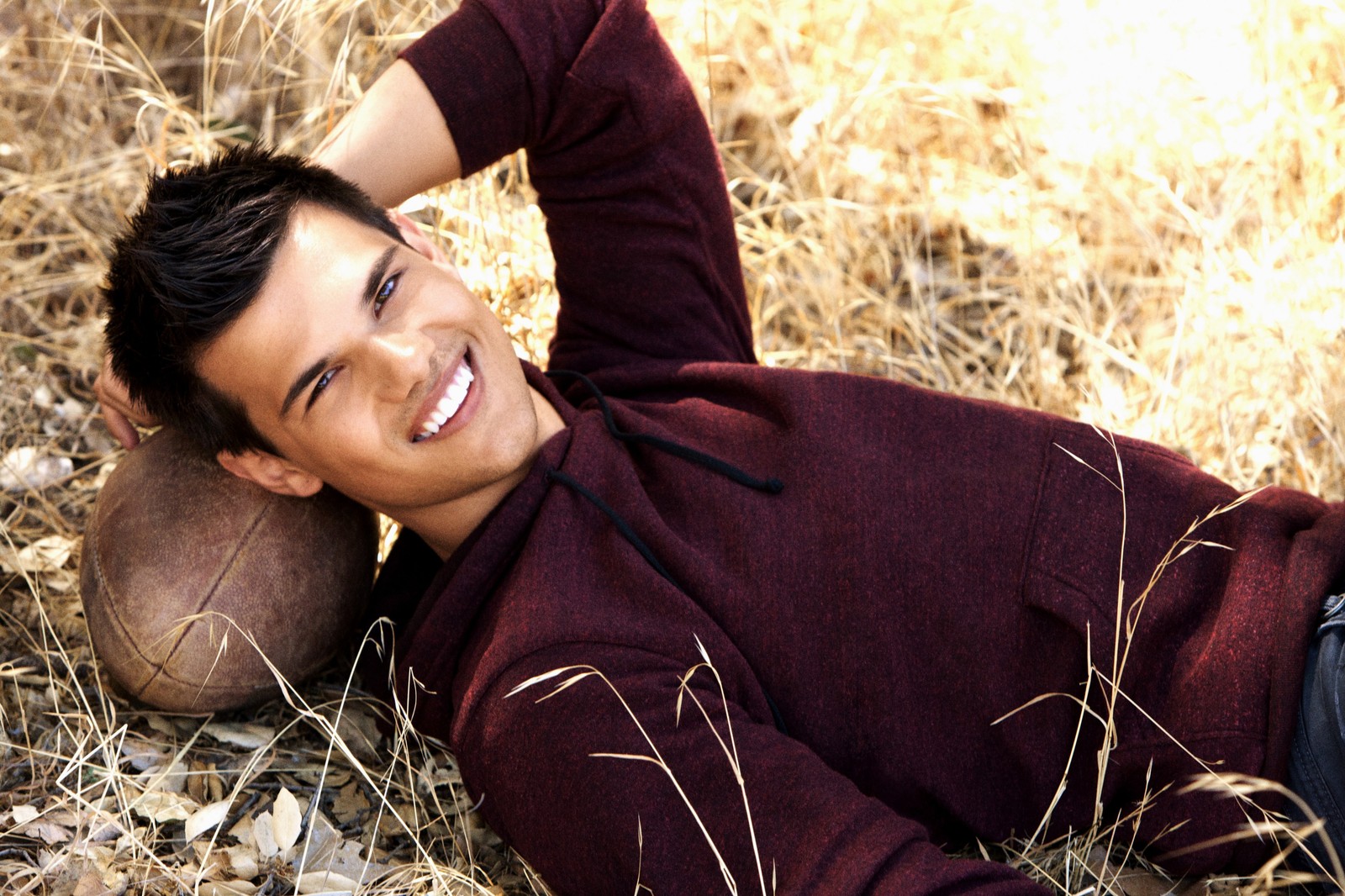 Arafed man laying on the ground with a football in his hand (taylor lautner, the twilight saga, twilight, grass, celebrity)