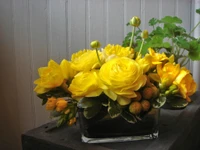 Arreglo floral vibrante amarillo con ranúnculos y follaje decorativo