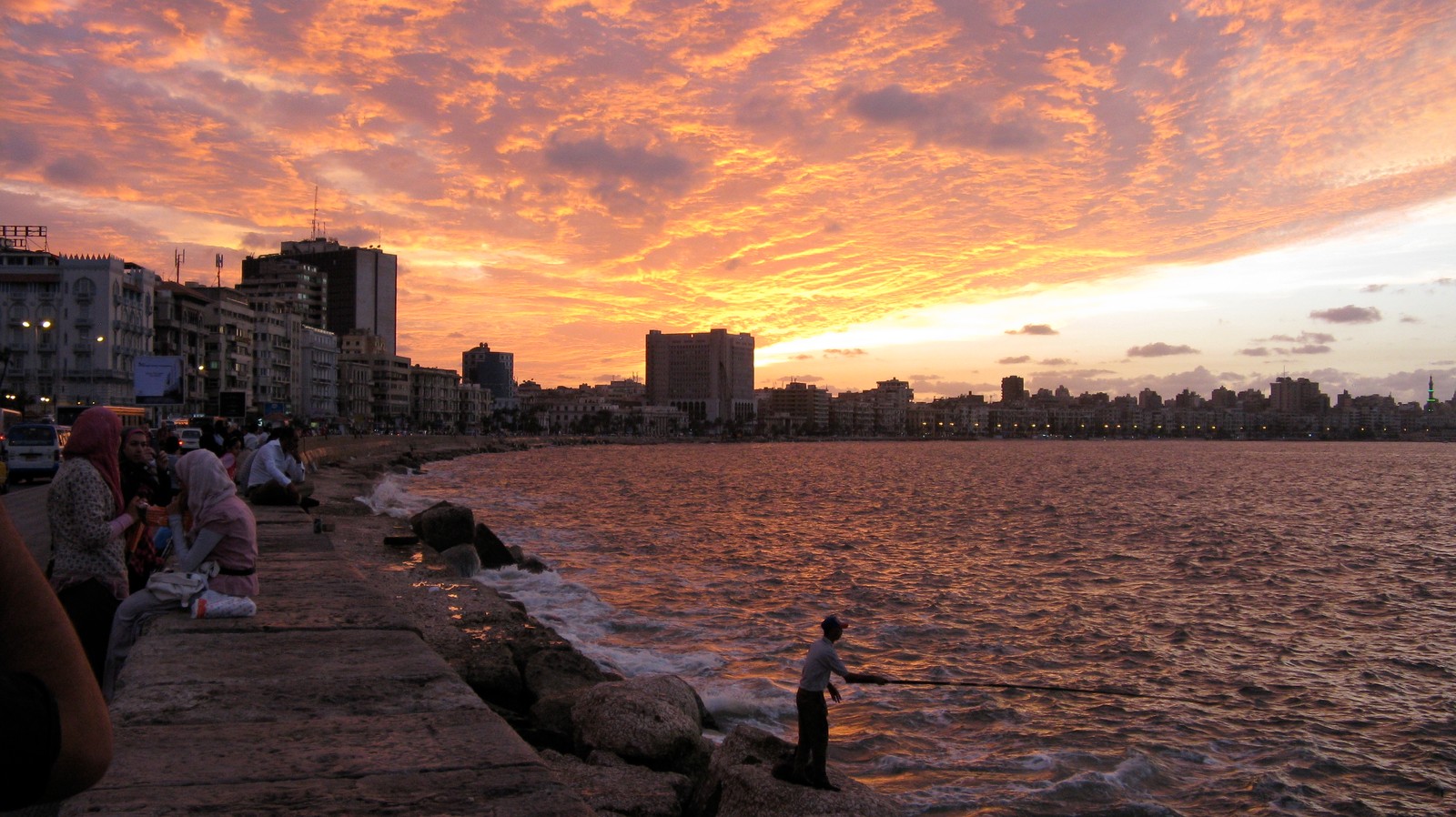 Pôr do sol sobre a água com pessoas em pé na beira do píer (por do sol, água, nuvem, horizonte, anoitecer)