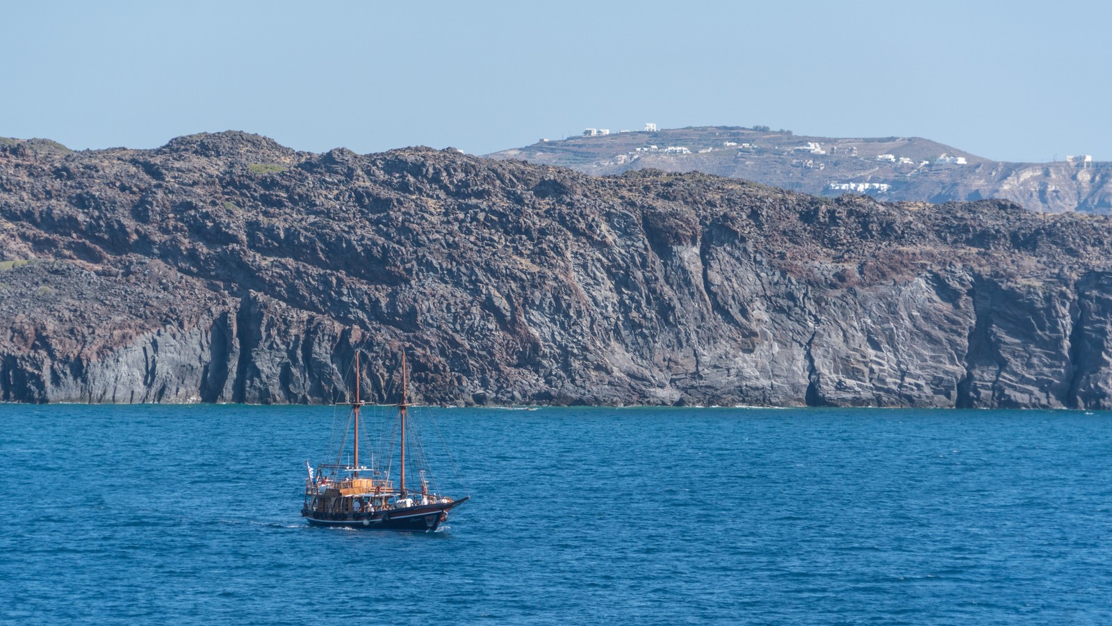 Um barco na água perto de um penhasco rochoso (mar, costa, formas costeiras e oceânicas, lago, oceano)