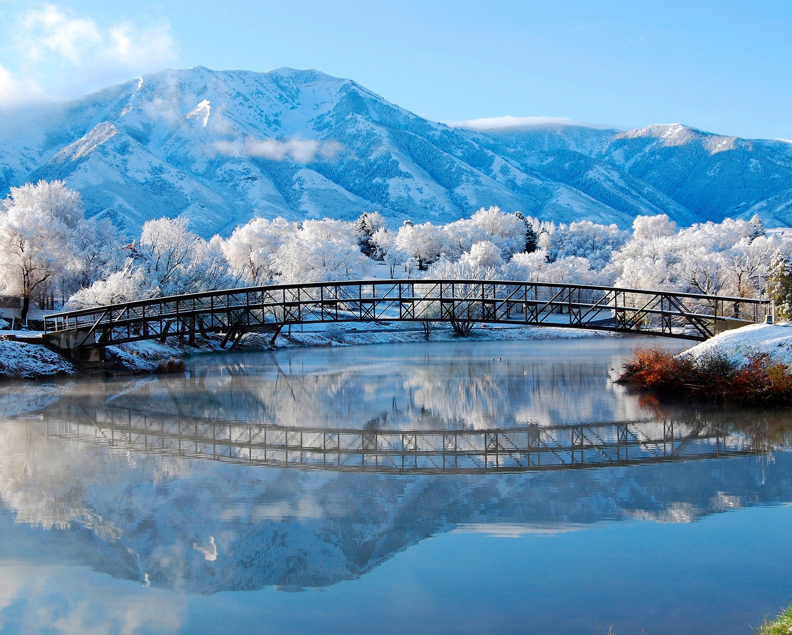 Paisaje nevado con un puente sobre un río y una montaña al fondo (natur azul, lago, montaña, nieve, invierno)