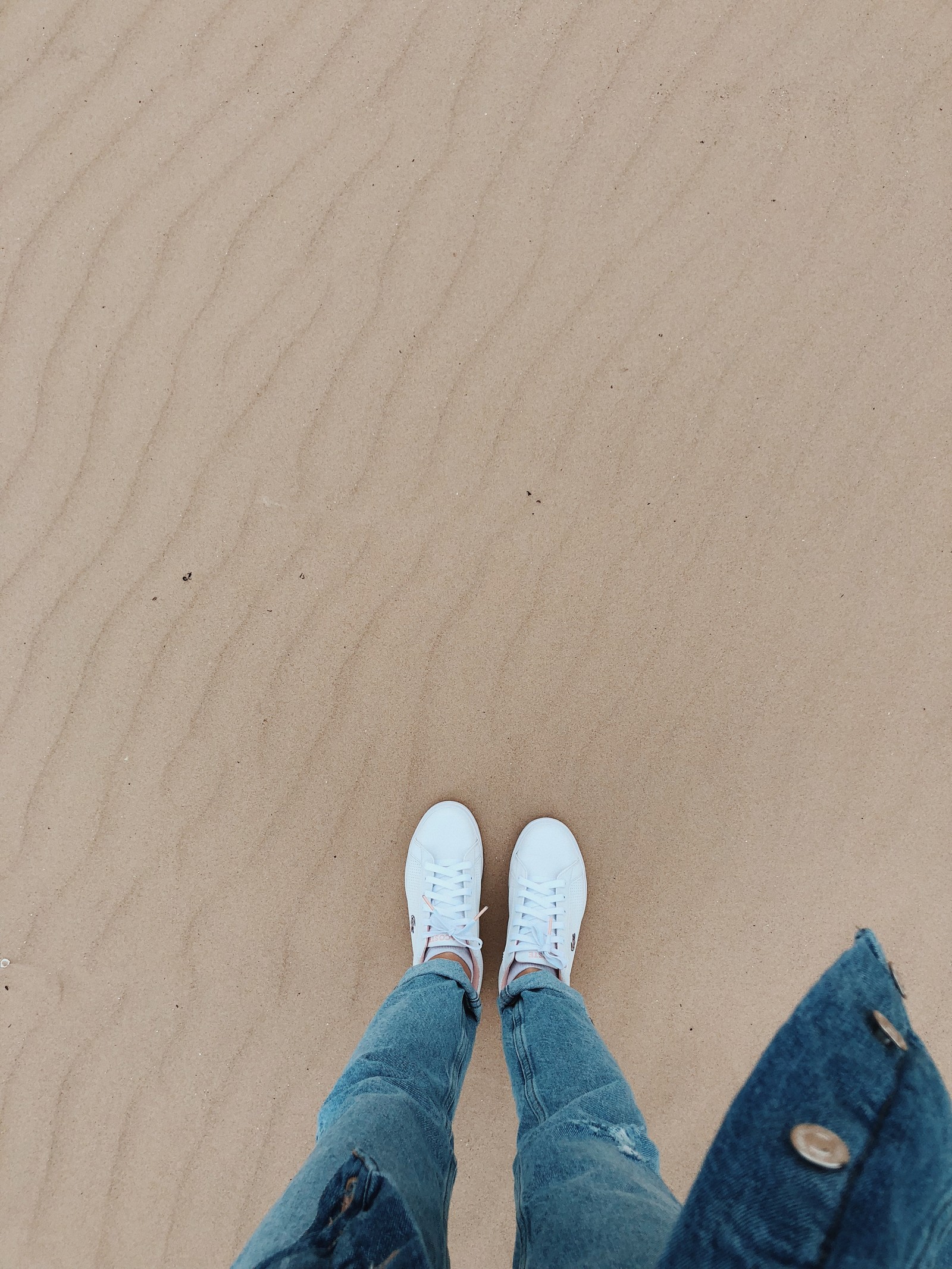 Someone is standing on a sandy beach with their feet in the sand (sand, clothing, human, leg, natural environment)