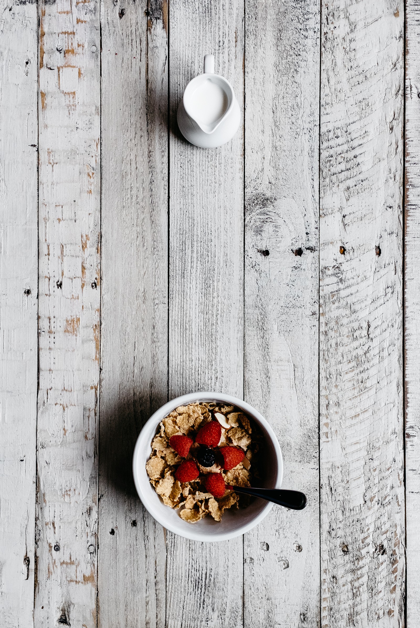 There is a bowl of cereal with strawberries and a spoon (breakfast cereal, breakfast, milk, food, cuisine)