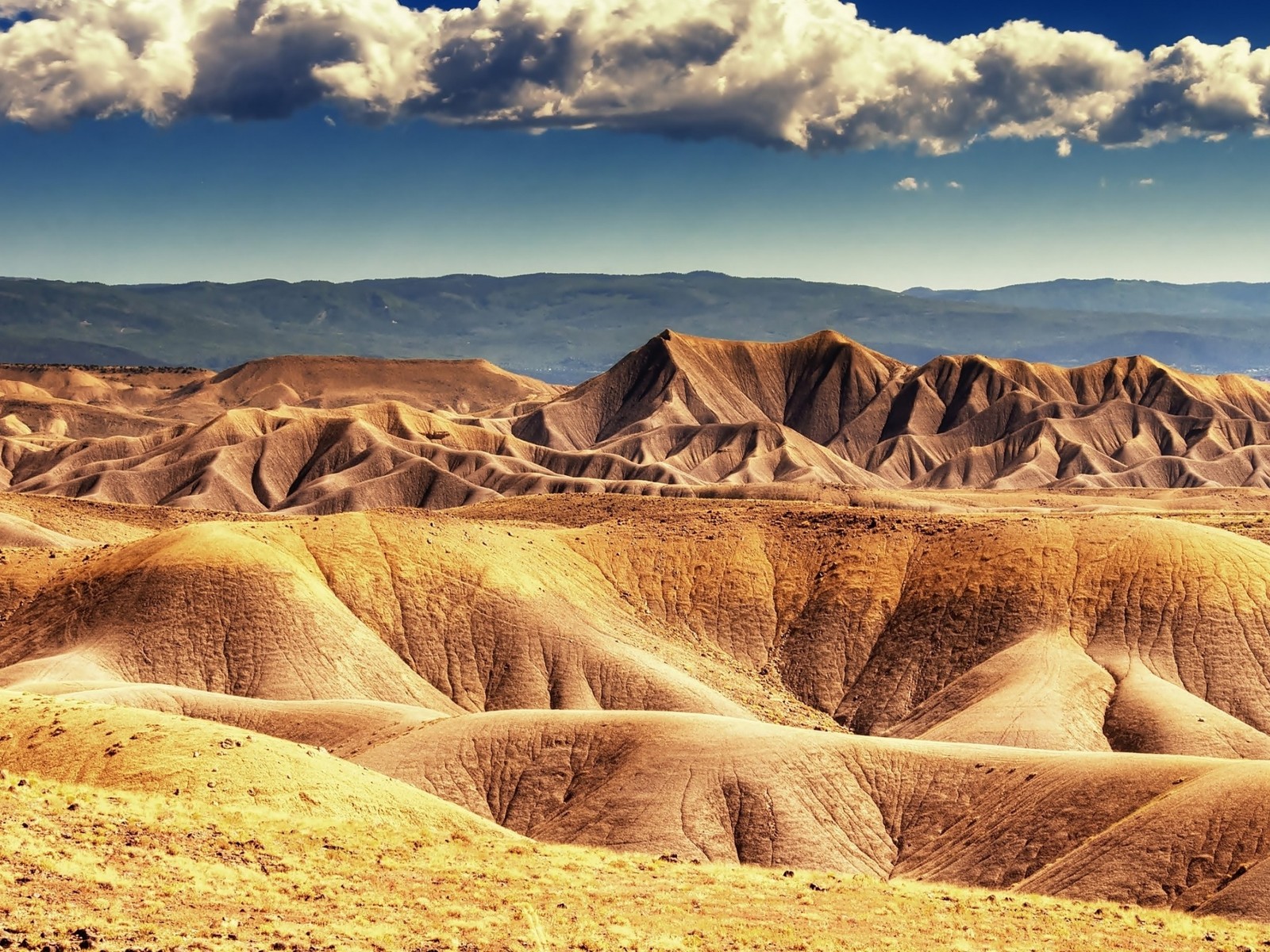 Paisaje desértico árabe con montañas y nubes a lo lejos (desierto, badlands, formas montañosas, geología, formación)