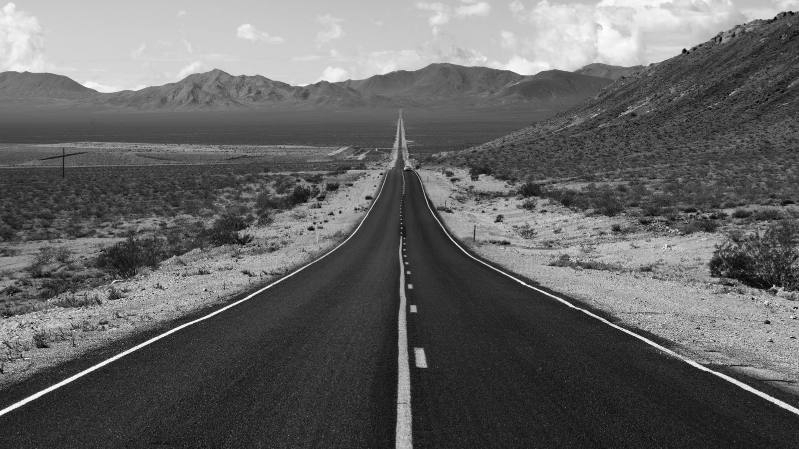 Foto en blanco y negro de una larga carretera en medio del desierto (nube, montaña, planta, superficie de la carretera, asfalto)