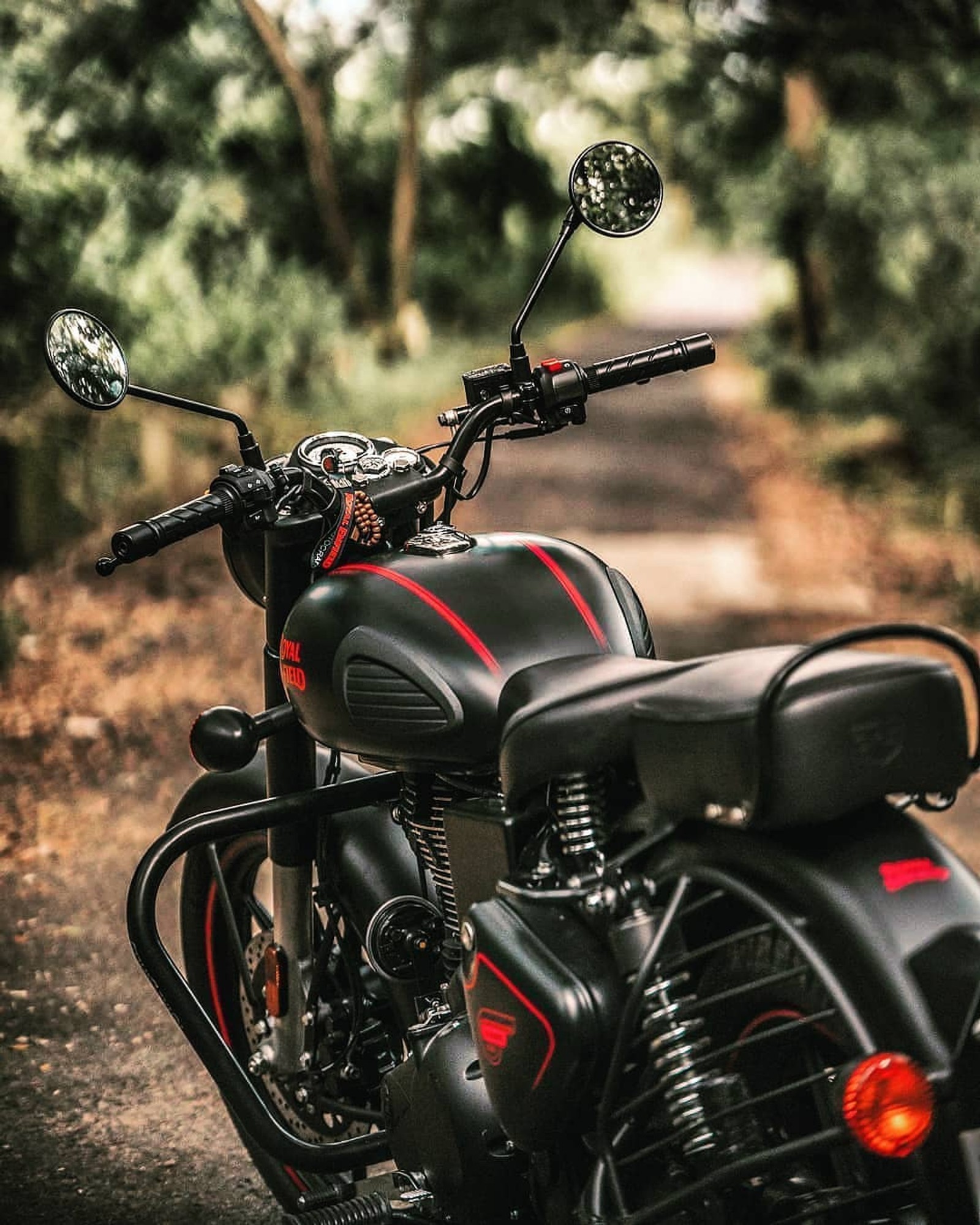 There is a motorcycle parked on a dirt road in the woods (bullet, king, mirzapur, royal)