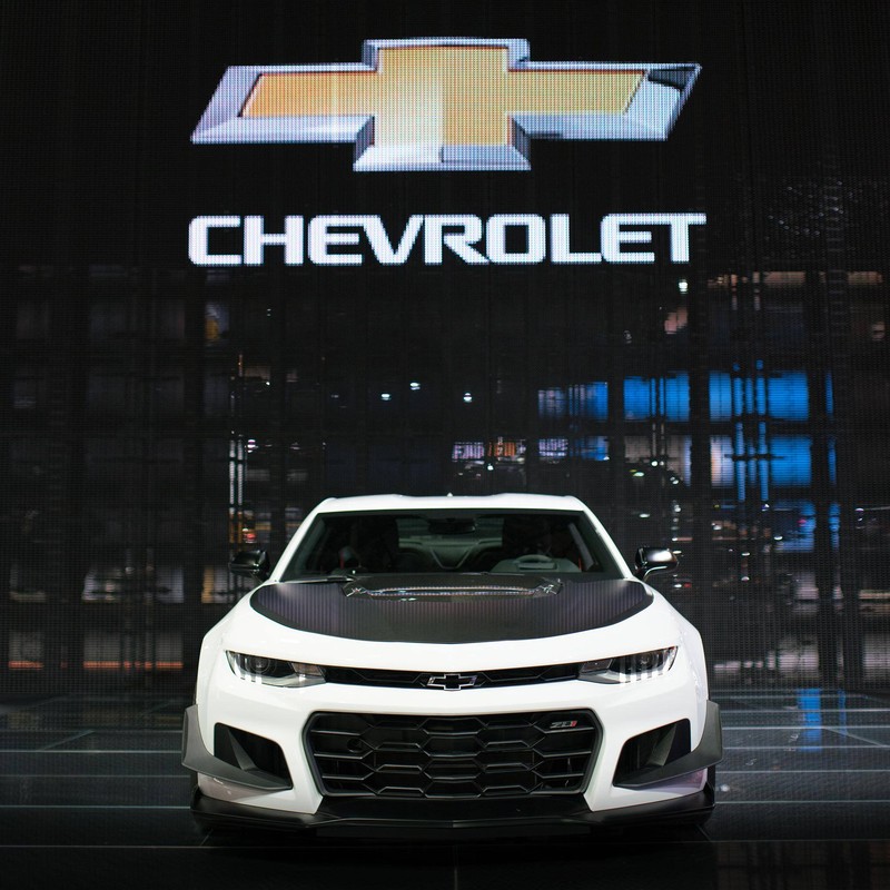 Логотип chevrolet motor corporation на стене с белым автомобилем. (2018, чёрный, camaro, машина, chevrolet)