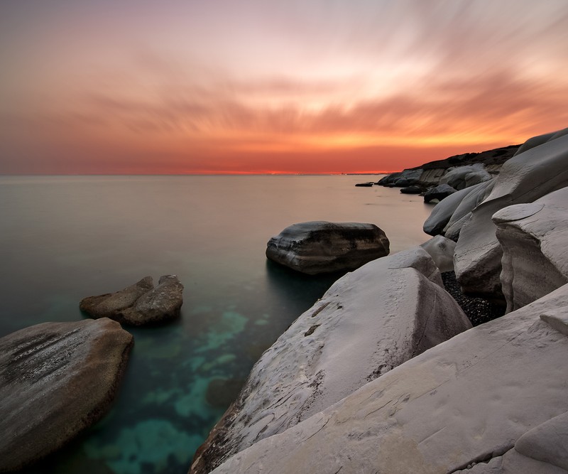 Размытый вид на каменистый пляж с закатом на заднем плане (закат, white rocks)