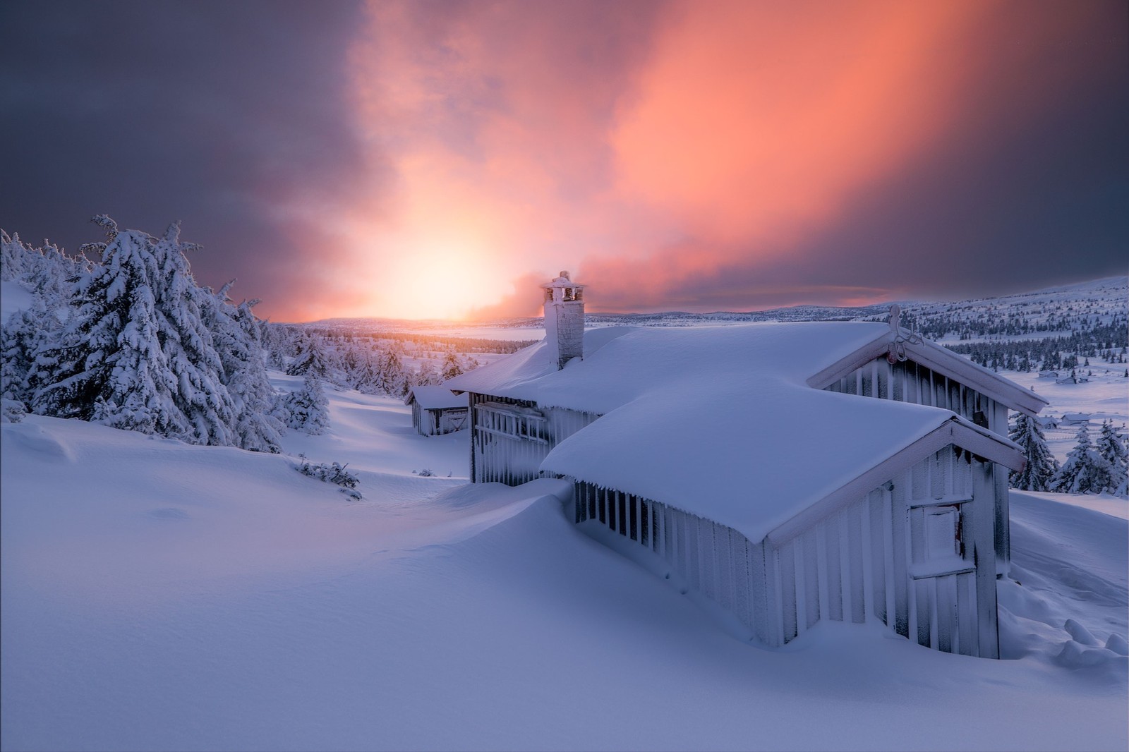 A snow covered cabin sits on a snowy hill with a sunset in the background (snow, winter, freezing, atmosphere, mountain range)