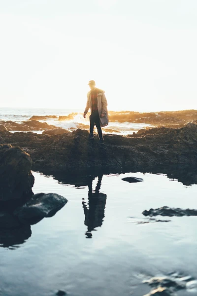 Silhouetted Figure on Rocky Coastline Reflecting in Tide Pool at Sunset