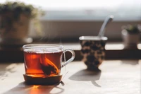 Xícara fumegante de chá Earl Grey em uma caneca de vidro, colocada sobre uma mesa de madeira com um fundo desfocado.