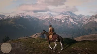 Ein Cowboy zu Pferd blickt über eine atemberaubende Berglandschaft in Red Dead Redemption 2.