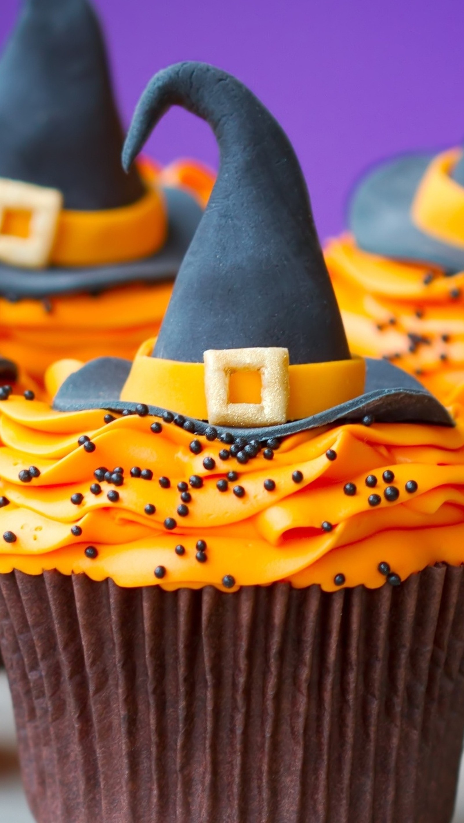 Há três cupcakes com cobertura laranja e chapéus pretos neles (cupckaes, halloween, chapéu, bruxa)