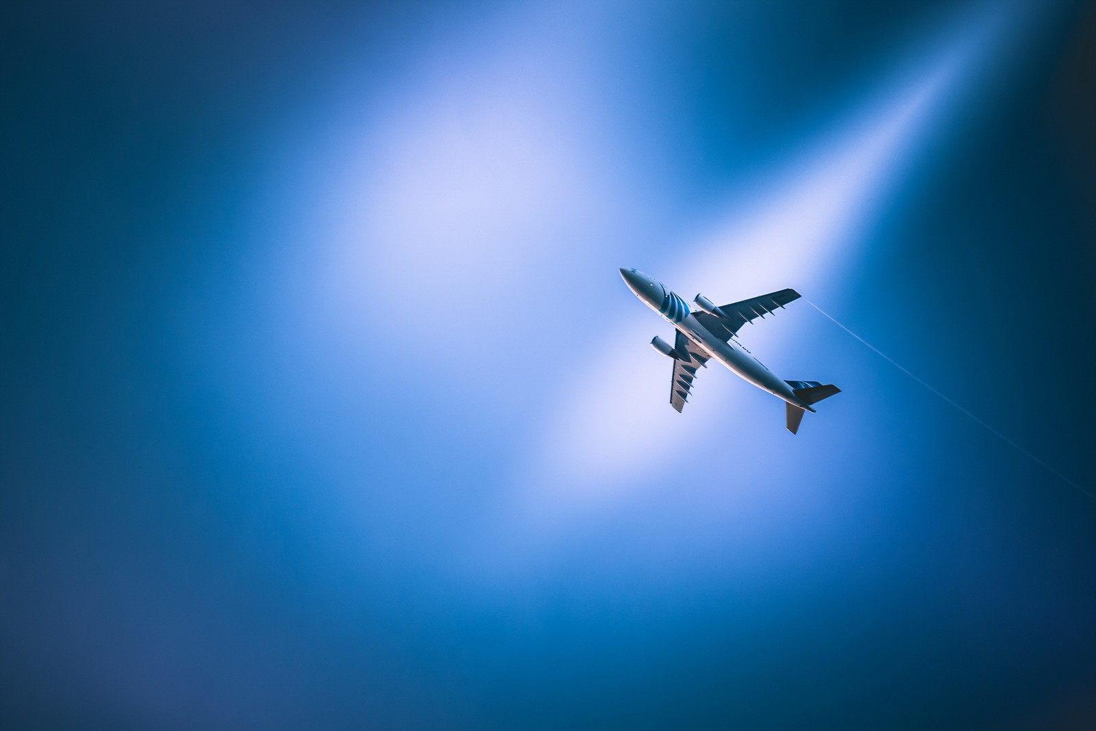 Há um avião voando pelo ar com uma luz brilhante vindo de trás (aeronave, aviação, viagem aérea, voo, azul)