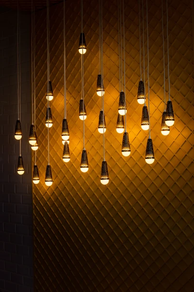 Contemporary chandelier featuring multiple hanging incandescent light bulbs against a textured yellow wall.