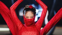 Jennie von BLACKPINK in einem auffälligen roten Outfit mit komplizierten Mustern, das einen intensiven und fesselnden Ausdruck zeigt und das Wesen der K-Pop-Kunst verkörpert.