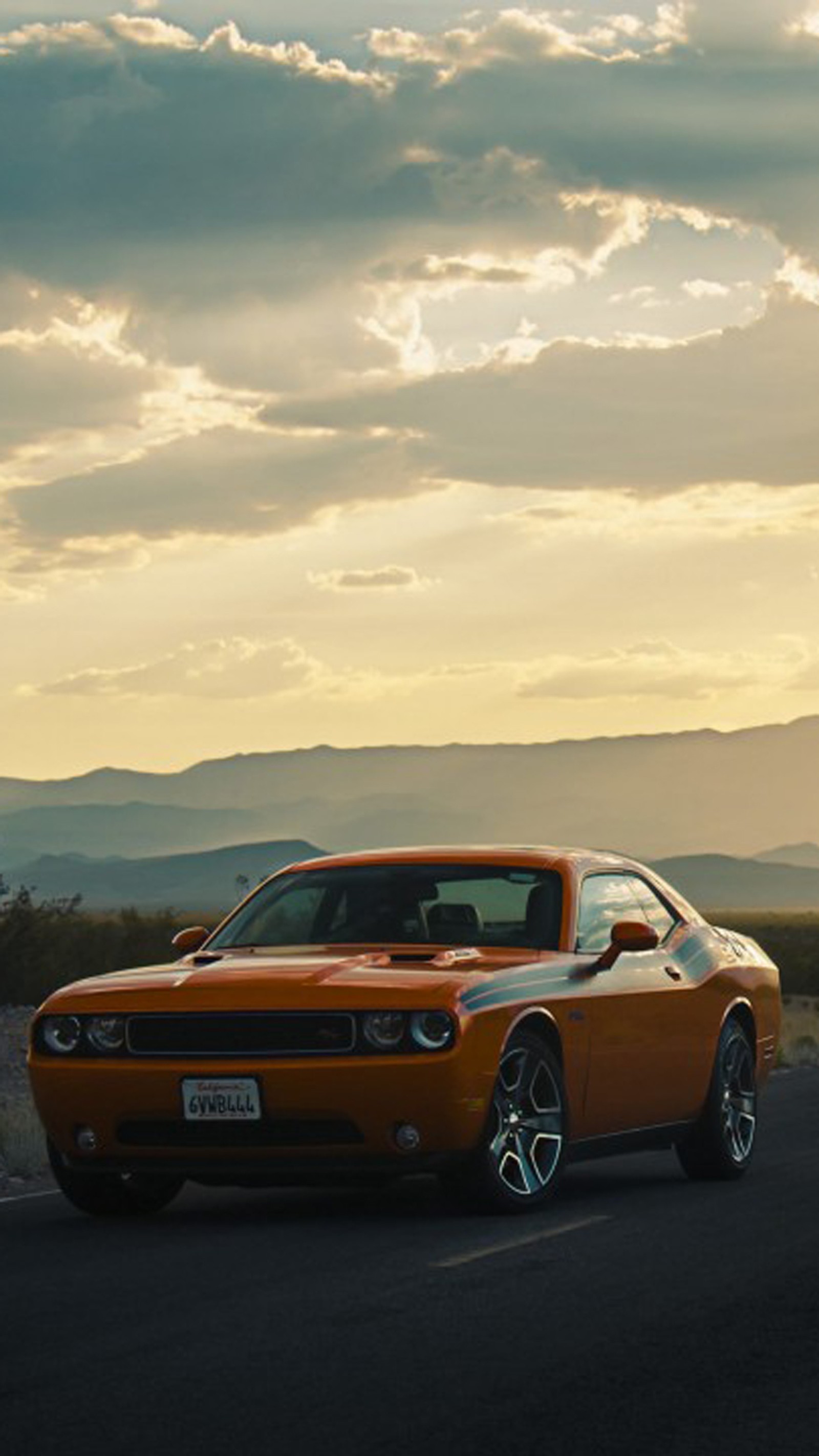 Un coche naranja conduciendo por un camino con montañas de fondo (estadounidense, coche, retador, dodge, motor)