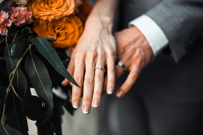 Mãos entrelaçadas exibindo alianças de casamento em meio a um buquê floral