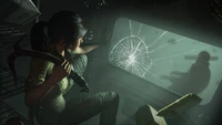 Lara Croft mira a través de una ventana de vidrio roto, proyectando una figura sombría en un oscuro entorno submarino, encarnando la emoción de la aventura en un videojuego.