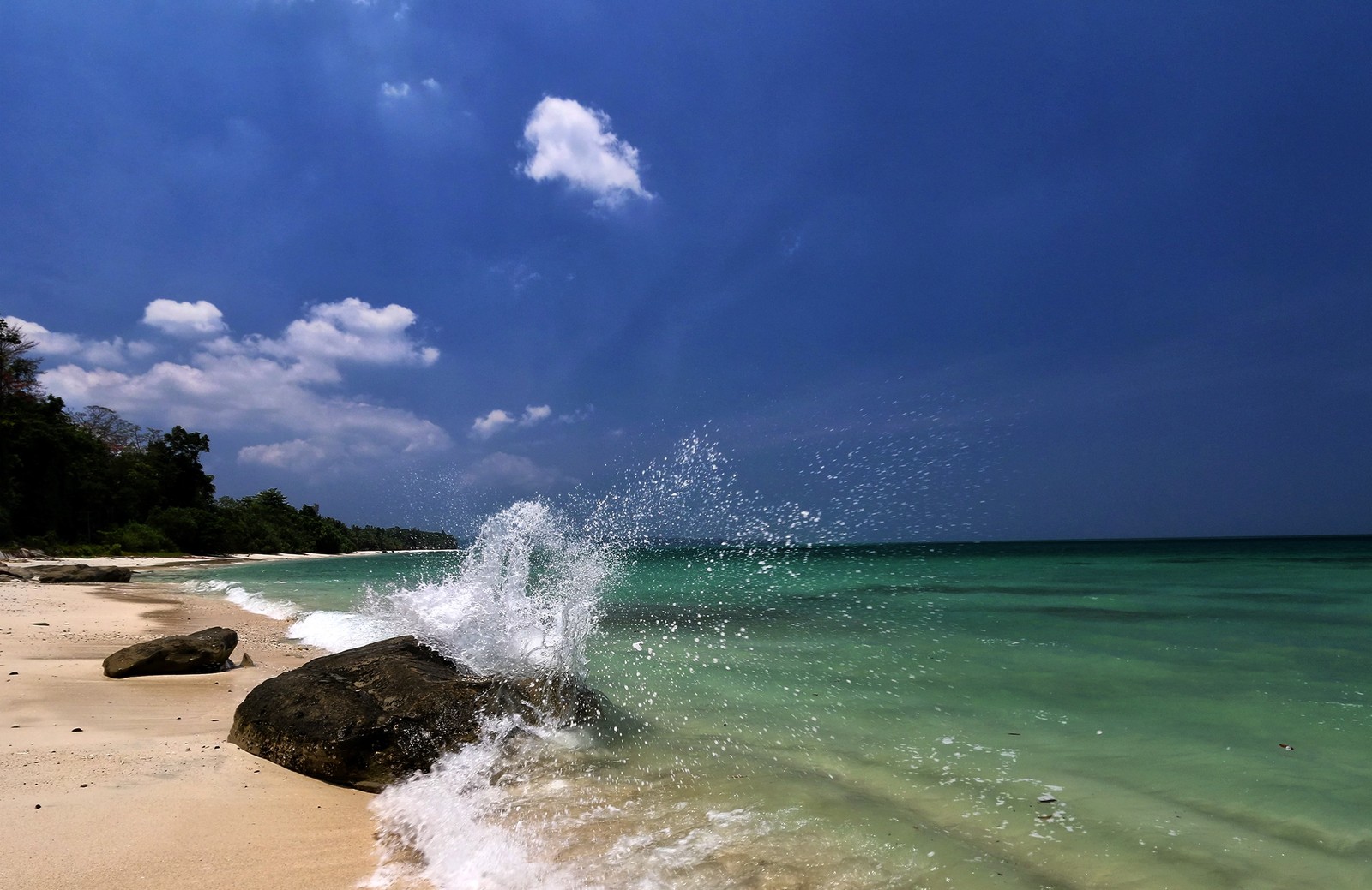 Vista de uma onda quebrando em uma praia com pedras (praia, mar, viagem, corpo de água, água)