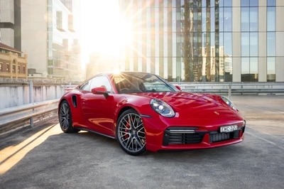 Porsche 911 Turbo 2021 en rouge frappant, capturé avec un arrière-plan urbain ensoleillé.