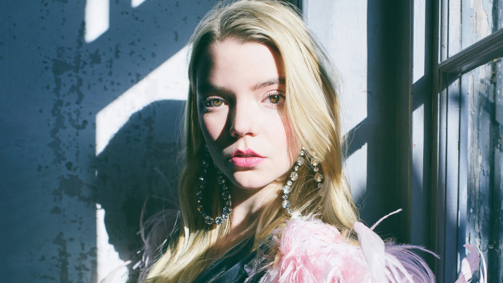 Mujer árabe con cabello largo rubio y aretes de pie junto a una ventana (anya taylor joy, rubia, actriz, mujer, chicas)